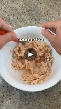 two hands holding a white bowl filled with shredded meat and carrots on top of a counter