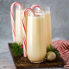 three glasses filled with milk and candy canes on top of a wooden tray next to christmas decorations