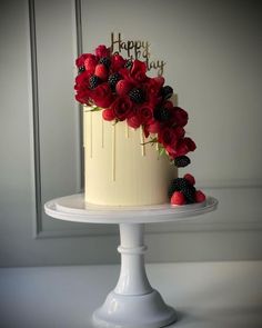 a white cake with red flowers and blackberries on top is sitting on a pedestal