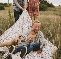 two young boys sitting on top of a blanket in a field next to an adult