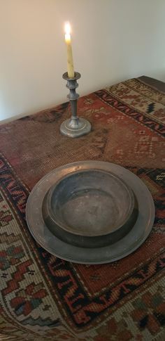 a lit candle is sitting on top of a table with a silver plate and bowl