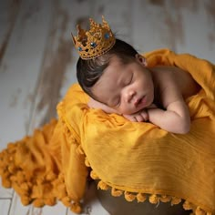 a newborn baby wearing a gold crown is sleeping on a yellow blanket in a bowl