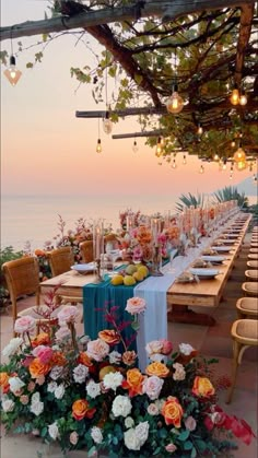 an outdoor dining table set up with flowers and greenery on the tables, overlooking the ocean