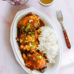 a white plate topped with meat covered in gravy and rice next to a cup of tea