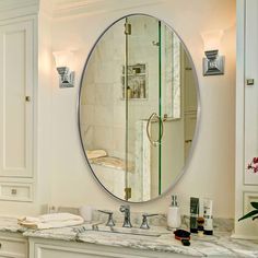 a bathroom with a large round mirror and marble counter top, along with white cabinets