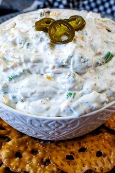 a white bowl filled with ranch dip surrounded by crackers and jalapenos