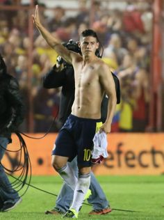 a shirtless soccer player waves to the crowd as he walks off the field with his arm in the air