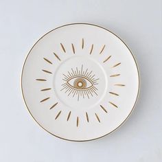 a white and gold plate with an evil eye on it's center, against a gray background