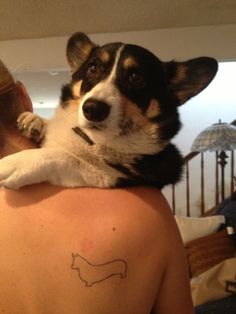 a woman holding a small dog on her back while she has a tattoo on her shoulder