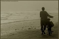 a man riding a bike on top of a sandy beach next to the ocean in black and white