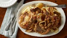 a white plate topped with pasta and meat covered in gravy on top of a wooden table