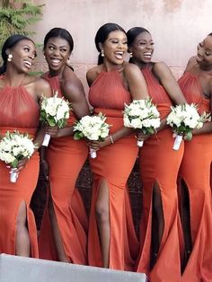 a group of women standing next to each other wearing orange dresses and holding bouquets