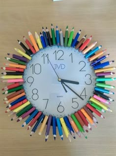 a clock made out of colored pencils on a wooden table with the time twelve o'clock