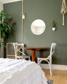 a bedroom with green walls, white furniture and a round mirror hanging on the wall