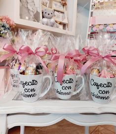 three coffee mugs with pink bows and chocolate candies in them sitting on a table