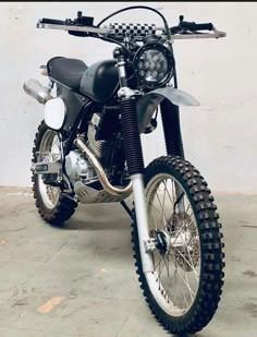 a black and white motorcycle is parked on the cement floor in front of a wall