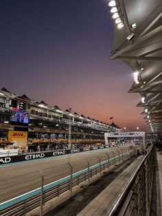 an empty race track at night with the lights on and people watching from the stands