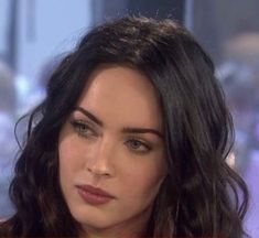 a close up of a person with long hair and wearing a red shirt on the set of an interview