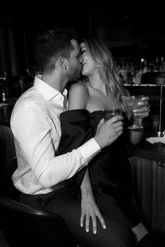 a man and woman sitting next to each other at a bar with drinks in their hands