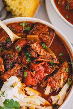 two bowls filled with stew and vegetables on top of a white tablecloth next to a piece of bread