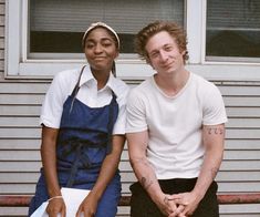 two people sitting next to each other in front of a house