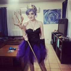 a woman dressed up in a costume holding a wand and posing for the camera while standing on a tile floor