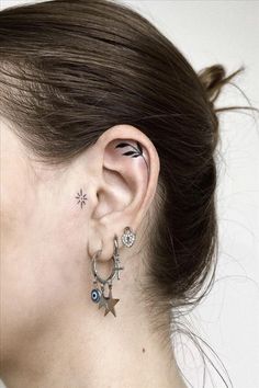 a woman's ear with two stars and an evil eye tattoo on her left side