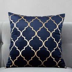 a blue and gold pillow sitting on top of a gray couch next to a white chair