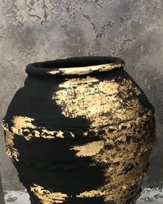 a large black and gold vase sitting on top of a white table next to a wall