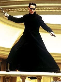 a man in a long black coat holding two swords on top of a balcony railing