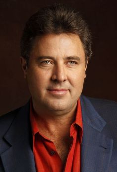 a man in a blue jacket and red shirt posing for a photo with his eyes wide open