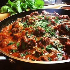 a pan filled with meatballs and sauce on top of a table next to vegetables