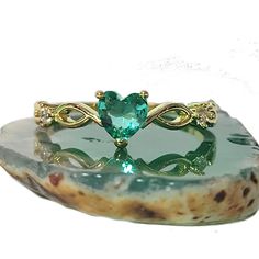 a green heart shaped ring sitting on top of a rock