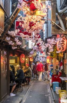 people sitting at tables in an alleyway with cherry blossom hanging from the ceiling above them