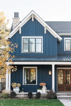 a blue house with white trim and brown doors is shown in the fall season,