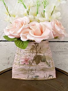 pink and white flowers are in a vase on a wooden table next to a wall