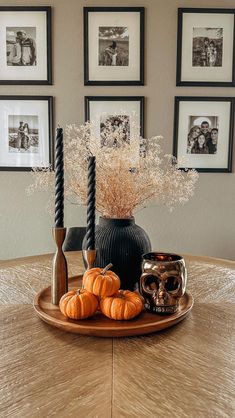 a wooden table topped with a black vase filled with flowers and pumpkins next to candles