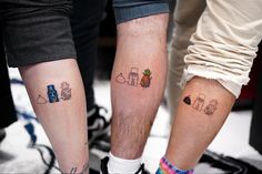 two people with matching tattoos standing next to each other on their legs, one has an apple and the other has a pineapple