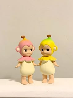 two small figurines are standing next to each other on a white surface with a gray wall in the background