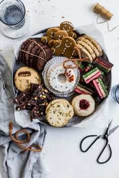 an assortment of cookies and pastries on a platter with scissors, napkins and glasses