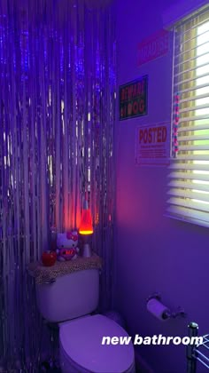 a bathroom decorated in purple and white with lights on the wall, toilet and window