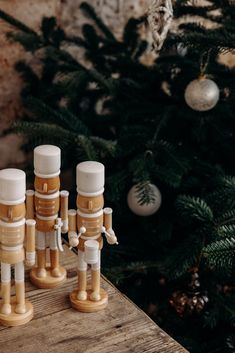 three wooden toy figures are standing on a table next to a christmas tree with ornaments