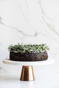 a cake with rosemary sprigs on top is sitting on a white plate and gold stand