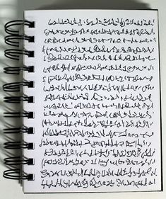 an open spiral notebook with arabic writing on the page and shadows coming from behind it