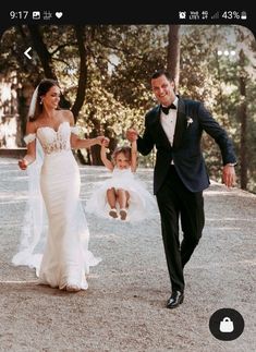 a bride and groom are holding hands as they walk through the park with their daughter