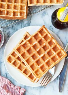 two waffles on a white plate next to butter, syrup and orange juice