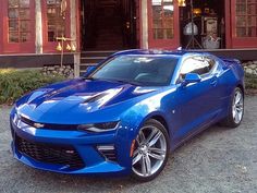 a blue chevrolet camaro is parked in front of a red building with two windows