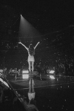 a black and white photo of a woman standing on stage with her arms in the air