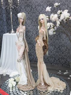 two mannequins dressed in long gowns and dresses with flowers on the table