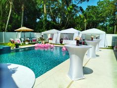 an outdoor pool with tables, chairs and umbrellas set up for a wedding reception